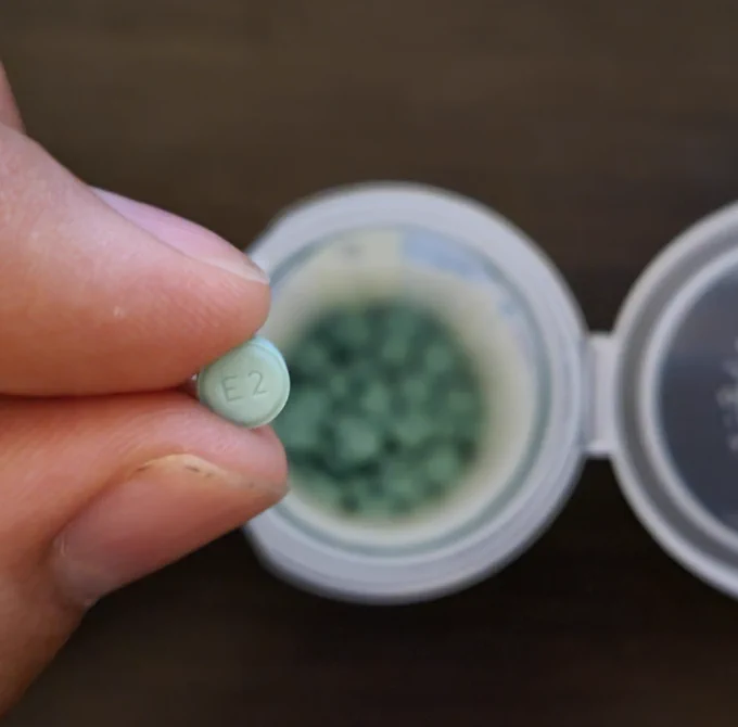 Me holding a pill of Estradiol with a bottle full of them in the background