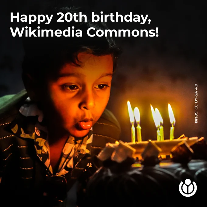 A young child leans forward to blow out four lit candles on a birthday cake, with the soft glow of the candlelight illuminating their face in a dimly lit room. Text says: Happy 20th birthday, Wikimedia Commons!