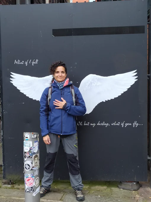 Foto de Rebeca Galán en Manchester. Está colocada delante de un mural en el que salen pintadas dos alas de su espalda. A los lados pone: "What if I fall. Oh but my darling, what if you fly"