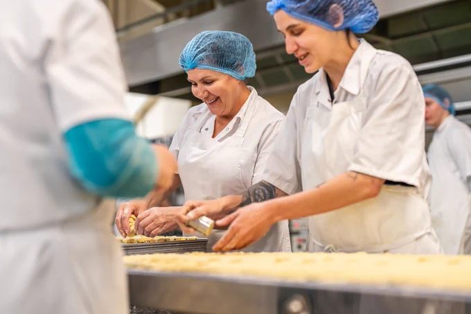 2 women in white uniforms and hair nets handling shortbread