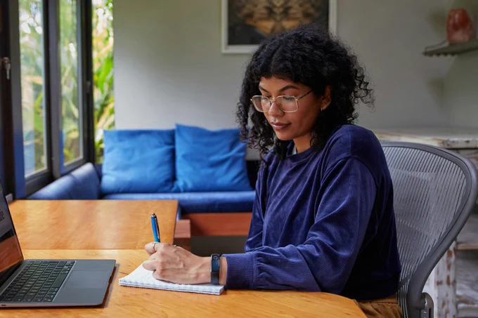 A person sat at a writing desk with a pen and notebook.