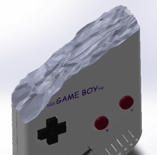 A cad model of the hand controller unit shell. It looks like the bottom half of a GameBoy which has been roughly cut at an angle of about 45 degrees just above the " " joypad button up towards the top left. The cut "face" has a computer generated surface that looks a bit like a stone has fractured in to a rough faceted surface.