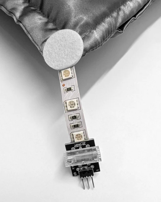 An exposed computer hard drive (HDD Toshiba MK2109MAT 2GB 5.4K IDE 2.5") rests on a silver satin royal pillow. The pillow has four tassels on the corners made from computer cables and connectors.