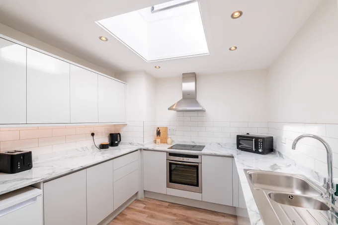 White U-shaped Kitchen with white and grey marble top. Black kitchen appliances and a large skylight in the middle of the room