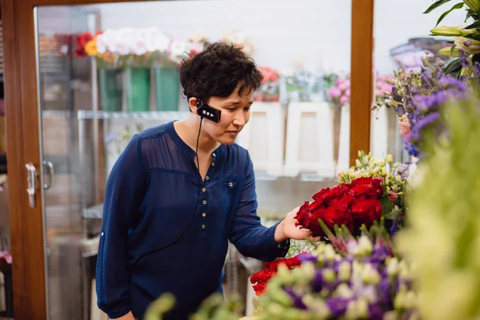Woman at a flower shop in front of flowers with her ARxVision headset on.