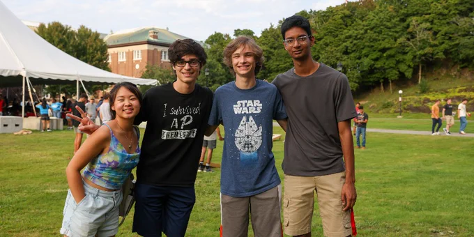 Four people posing for a photo at RPI's Welcome Fest with a grassy field and buildings in the background.
