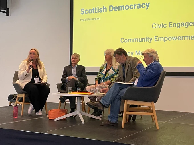 A group of people seated including Minister Ivan McKee for a conference panel discussion led by Pauline Smith Chief Executive of Development Trust Association Scotland