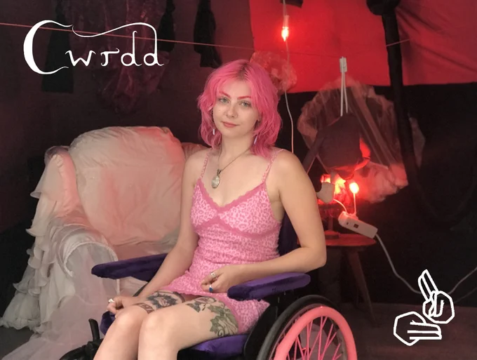 Image of a young woman in a wheelchair with bright pink hair wearing a bright pink dress. The image includes the BSLI logo in the bottom-right corner and text reading ‘Cwrdd’ in the top-left corner.