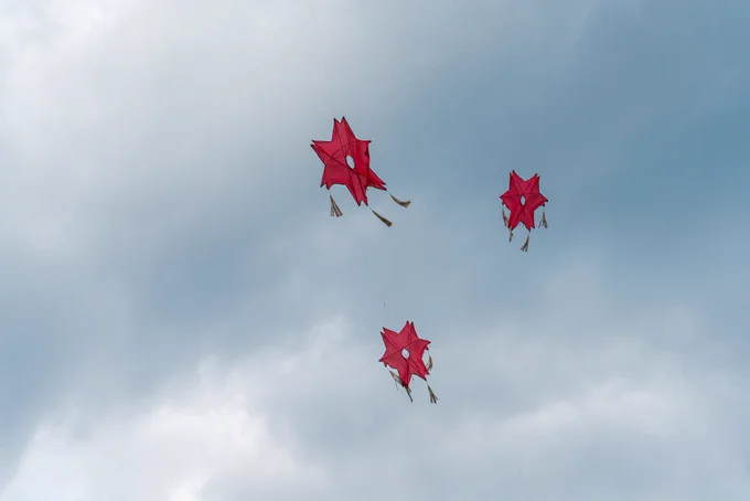 three red kites in the shape of six-sided stars fly in a cloudy sky.