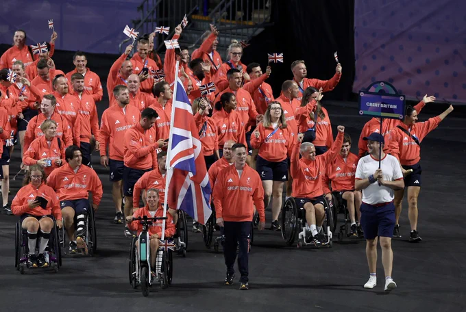 The team enter the ceremony holding the Union flag wearing red