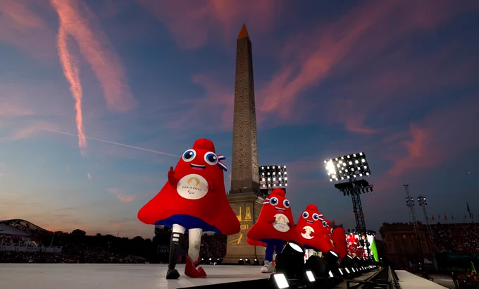 A line of Phruge mascots in front of the Place de la Concorde Obelisque with a gorgeous pink and blue sunset behingd them