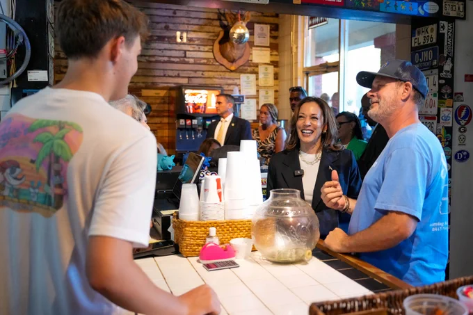 Vice President Kamala Harris smiling with patrons at a busy restaurant counter.