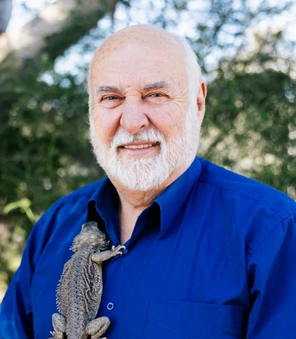 A man stands outdoors with a large lizard clinging to his shirt.