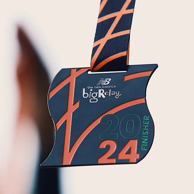 Close-up of the 2024 The Big Relay finisher medal, hanging by an orange ribbon with crisscross patterns.