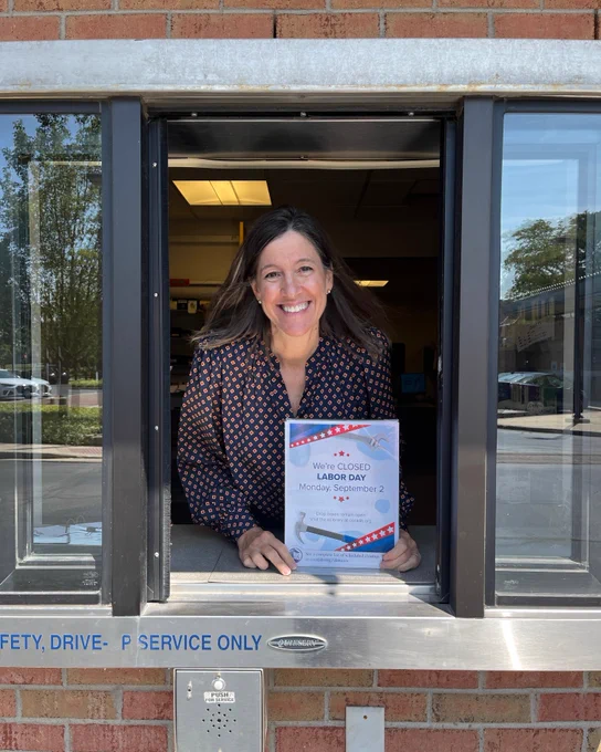photo of a staff member leaning out of the drive-up window holding a "We're closed for Labor Day" sign.