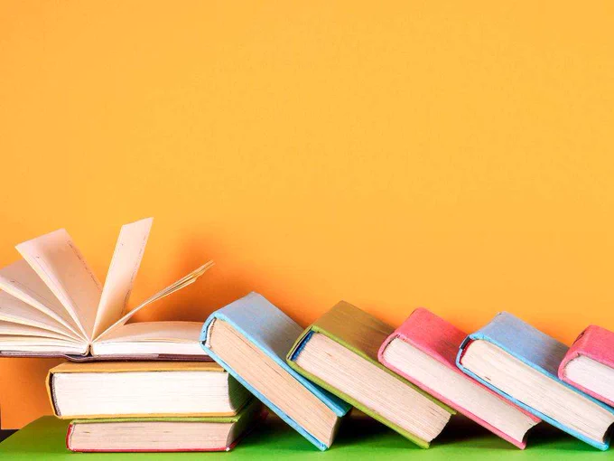 A collection of colorful books arranged horizontally with one open book on an orange background.