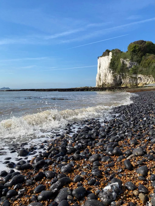 Pebbly beach with gentle waves lapping and white cliffs in the distance