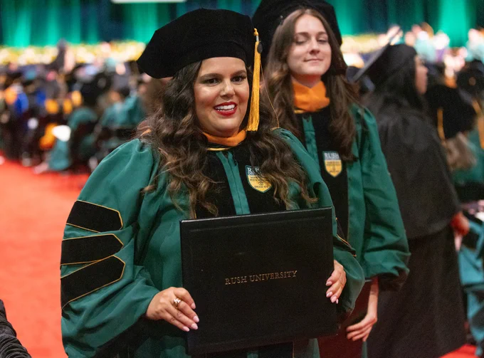 Delilah Flexas in regalia holding a diploma from Rush University, smiling proudly during the graduation ceremony.