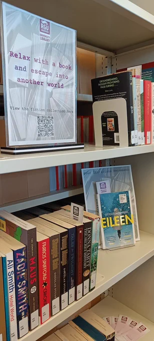 Close up of poster welcoming library users to "relax with a book and escape into another world " by fiction collection books