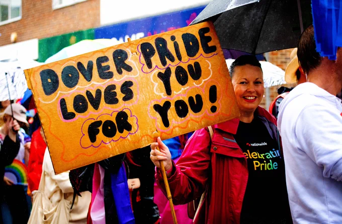 A marcher in the parade at Dover Pride 2024 holds up a sign that reads 'Dover Pride Loves You For You'.