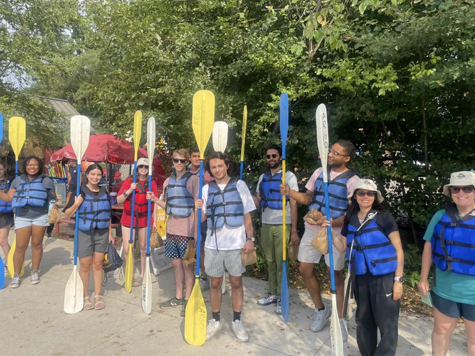 A group of people in blue life jackets with kayak paddles