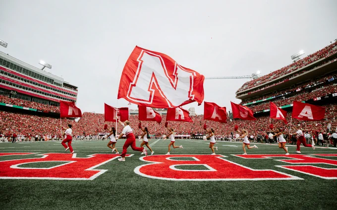 Husker Cheer members run flags spelling Nebraska across the field