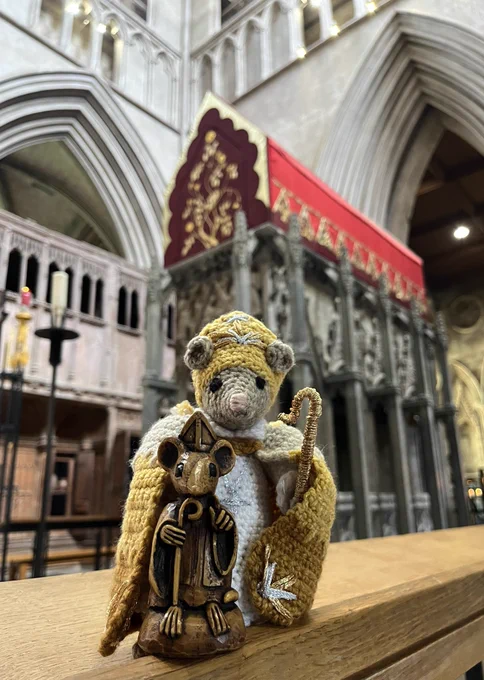 The two mouse bishops stand beside each other, one wooden and the other knitted, in front of the red-canopied shrine of St Albans.