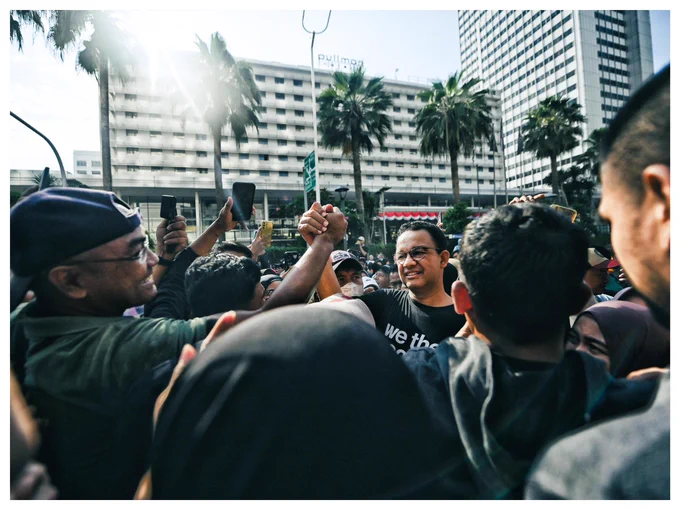 Anies bersalaman tinggi di udara dengan seorang pria di antara kerumunan orang-orang di CFD Jakarta.