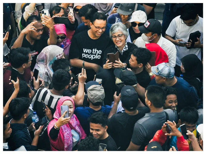 Anies Baswedan dikerubungi orang-orang yang ingin bersalaman atau berfoto dengannya di CFD Jakarta. Anies tampak memakai kaos hitam bertuliskan: “we the people”.
