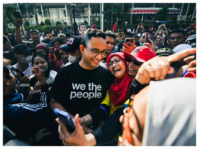 Beberapa ibu-ibu tampak tersenyum lebar berswafoto dengan Anies di CFD Jakarta. Anies memakai kaos hitam bertuliskan: “we the people”.