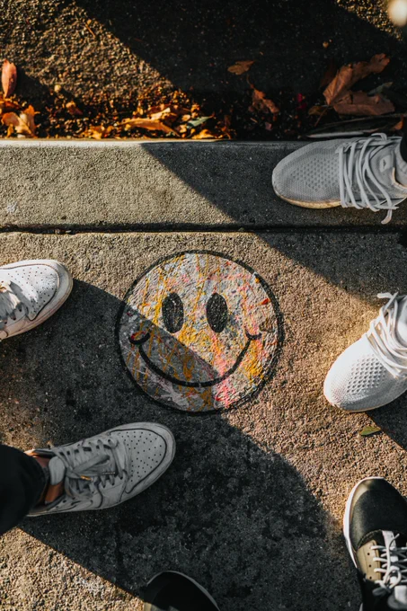 gray concrete ground with chalk smiley face and shoes of people standing around
