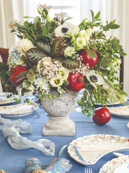 Alt text:
A flower arrangement with white blossoms and red apples tucked in an urn on a tabletop.