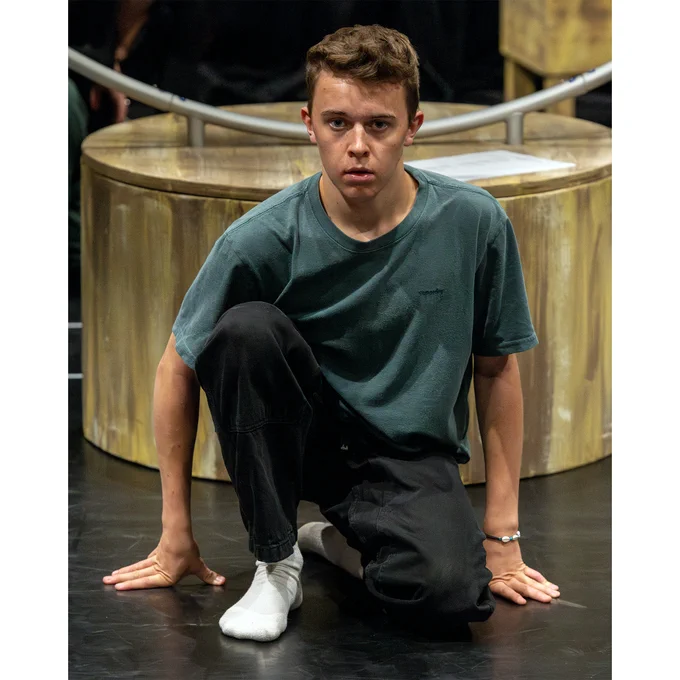 A young man on one knee and hands on stage staring straight ahead.