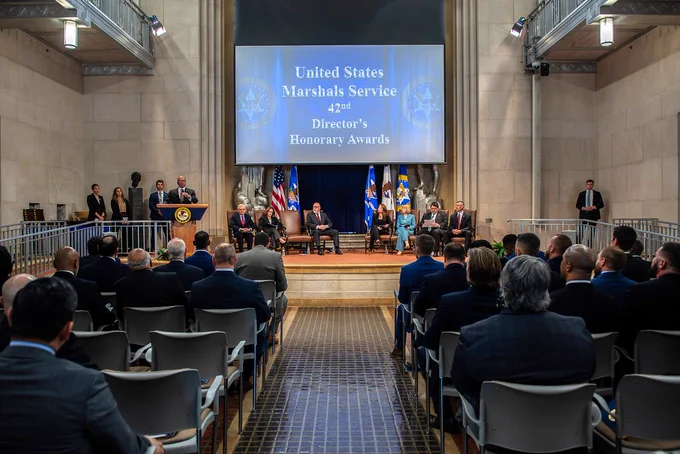U.S. Marshals Service staff are seated in front of a large projector screen that reads: "United States Marshals Service 42nd Director's Honorary Awards."