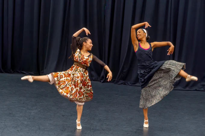 Two ballerinas dancing on a stage in floral dresses.