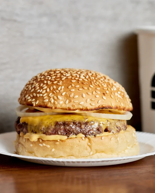 Cheeseburger with a sesame seed bun, a beef patty, melted cheese, and sauce on a white plate.