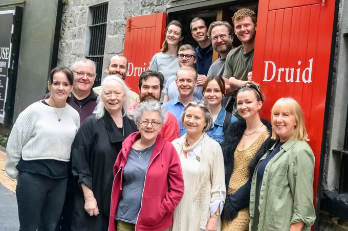 The cast and director of The House by Tom Murphy standing together for a group photo on Druid Lane in front of the red doors of The Mick Lally Theatre