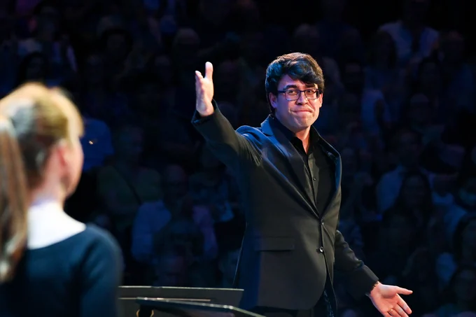 Conductor Owain Park gestures to the Singers, off-image, with his right hand.
