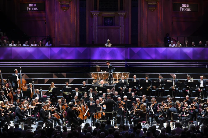 A wide shot of the Berliner Philharmoniker and conductor Kirill Petrenko performing on the Royal Albert Hall stage. Members of the audience sat in the choir stalls can be seen behind them. 