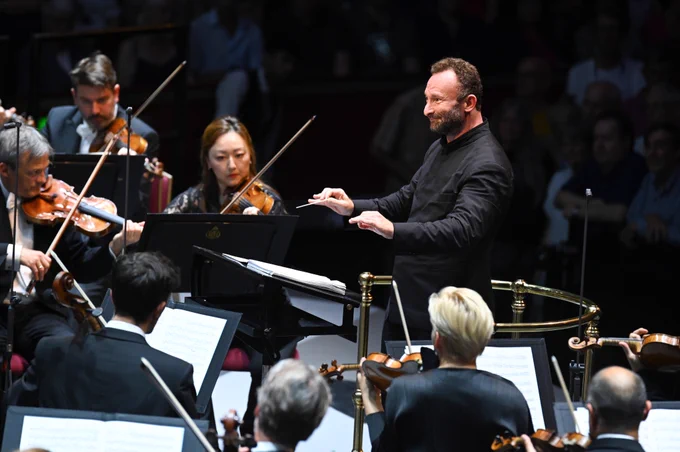 Kirill Petrenko conducts the Berliner Philharmoniker on the Royal Albert Hall stage. He is smiling.