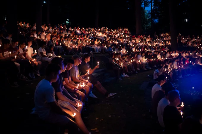 A large crowd of students seated in the Scott Outdoor Amphitheater at night. They are holding lit candles. 
