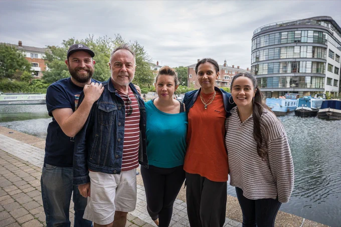 A photo showing five individuals standing in front of a quay while smiling in a huddle 