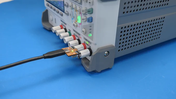 Bench power supply with an adapter plugged into it. The adapter is mostly orange. It has a USB-C connector with a cable attached. A cute green LED is on.