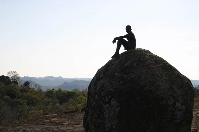 silhouette of a boy sitting on a large boulder, looking at the distant horizon - Matobos, Zimbabwe, 2004