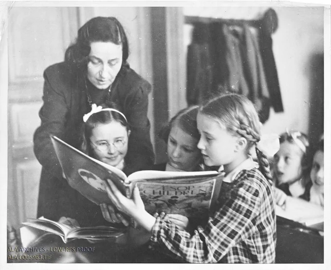 Black and white photograph of a woman and three girls reading a book.