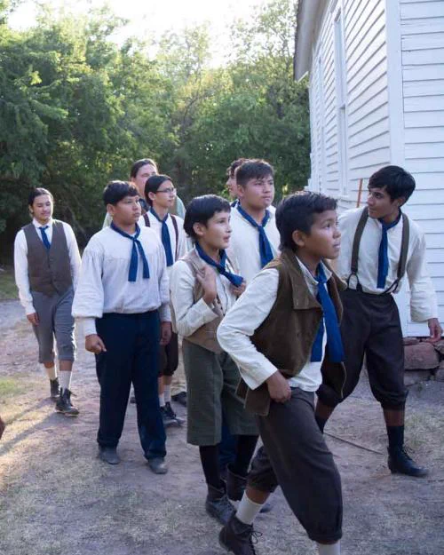 Image from a film: young actors dressed in short pants and white shirts as schoolboys