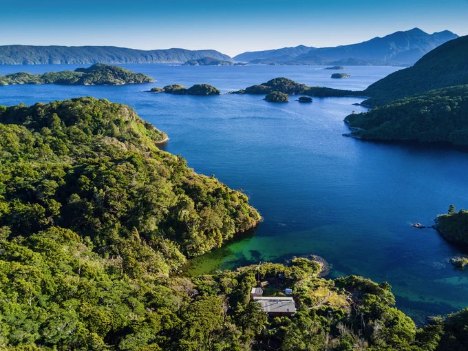 A hut among bush next to a bay in Fiordland, with islets in the background. Credit: Andrew Digby