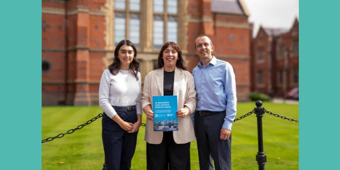Three people stand in front of a Queens University Belfast building, with the middle person holding a blue document. All are smiling to the camera. 
Left to right: Anna Montgomery, Research Assistant; Dr Marisa McVey, QUB School of Law; Dr David Russell, CEO of NIHRC. 