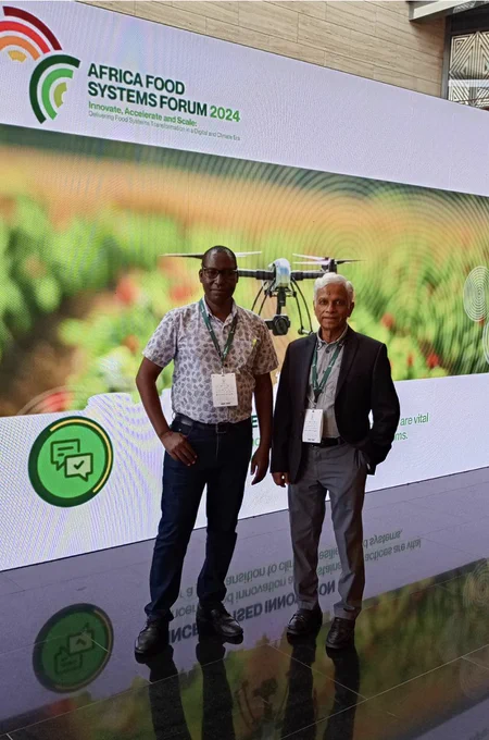 Fish Innovation Lab Africa Regional Coordinators Andrew Wamukota (left) and Sunil Siriwardena (right) stand in front of an Africa Food Systems Forum 2024 banner