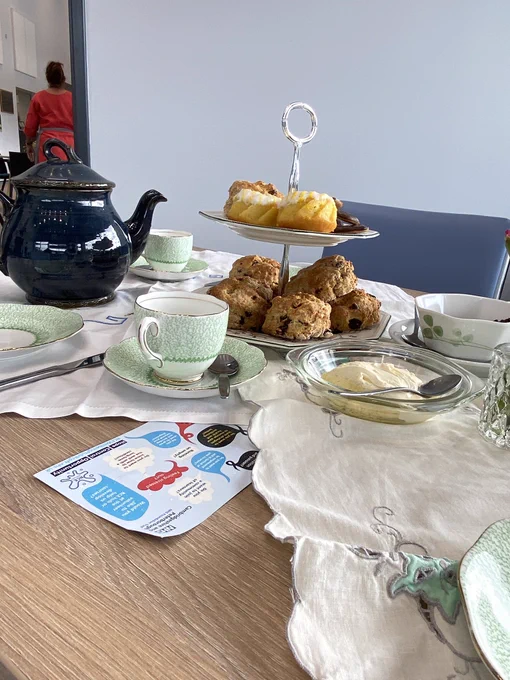 A beautifully presented table with fine china, scones, tea, and some RCE Wellbeing Hub promotional material
